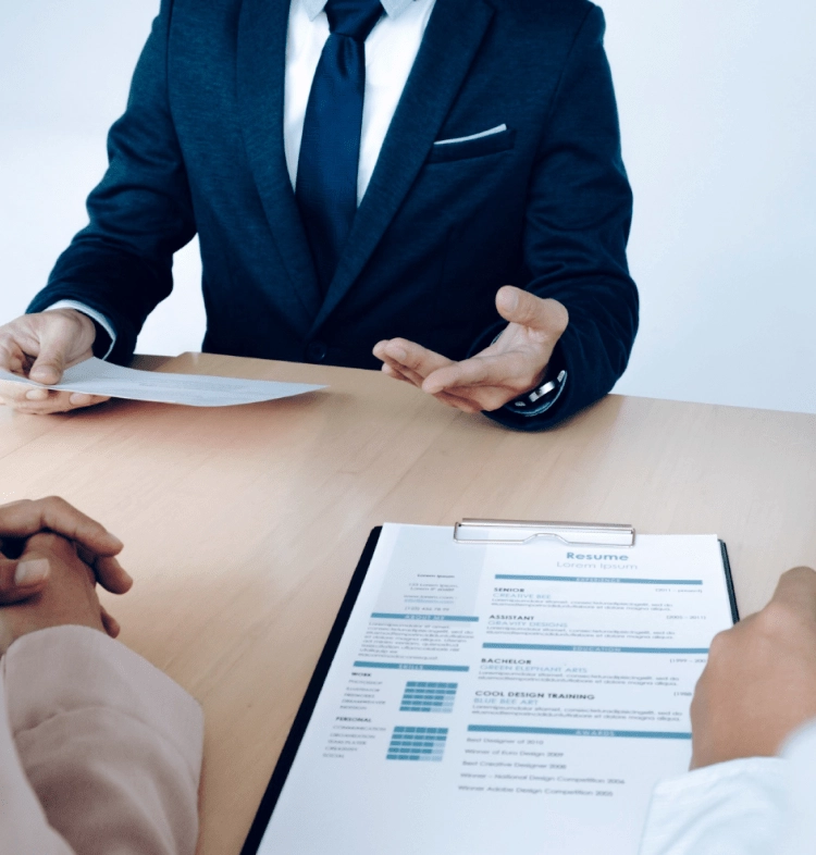 A professional interview scene with a man in a suit discussing a resume held by an applicant sitting across a wooden table.